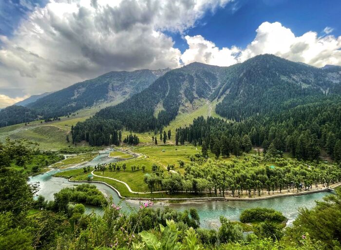 Scenic Kashmir landscape with snow-capped mountains, green valleys, and a lake on a 7-day Kashmir itinerary.